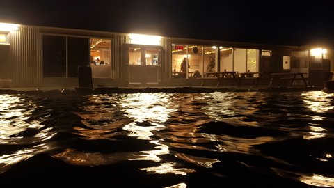 Illuminated waterfront kiosk at night, warm lights reflecting on dark water