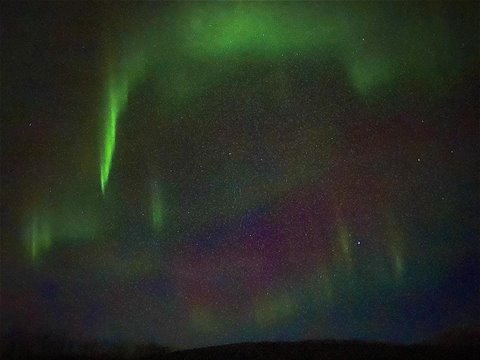 Green northern lights over dark hill, starry night sky, diary photo