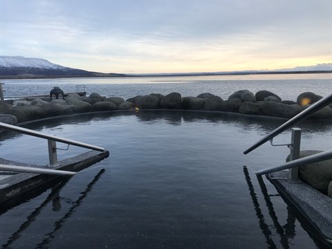 Hot pool with metal handrails overlooking a lake and snowy mountains