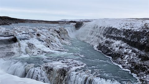 Icy waterfall between snowy rocks, milky water flows through the canyon, diffuse winter light