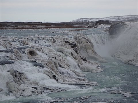 Frozen waterfall with glacial water, frost-covered rocks, grey winter sky above
