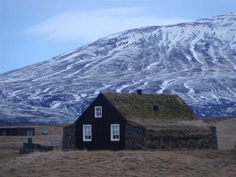 Stone house with grass roof, snowy mountain behind, cold light