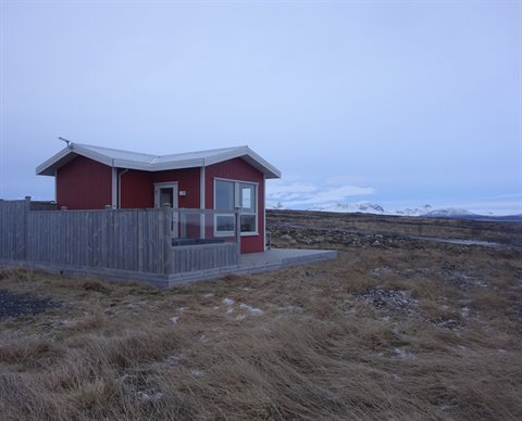 Red wooden cabin on barren ground, wooden fence, snowy mountains, cold light