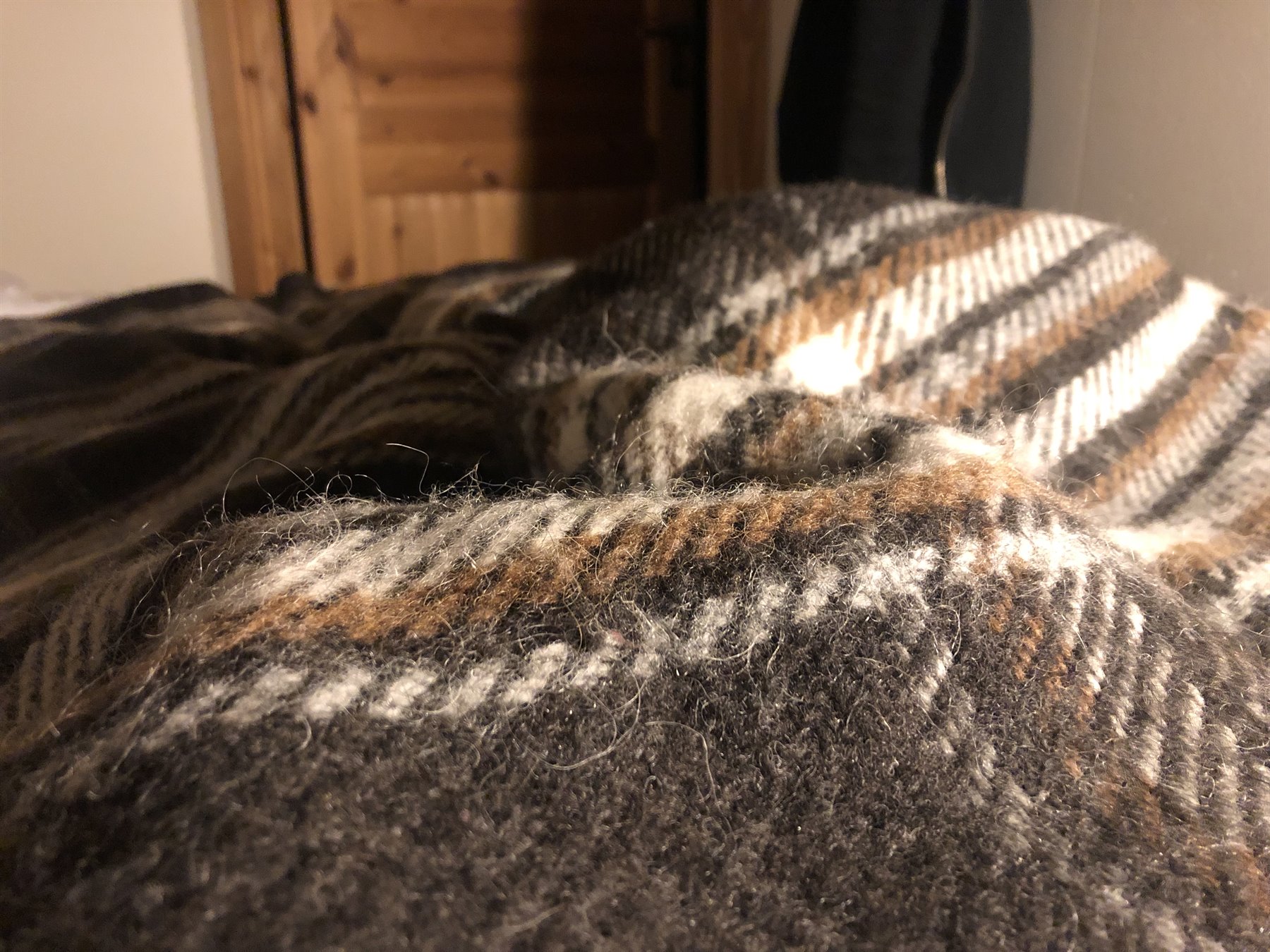 Wool blanket with brown stripes on a bed, warm indoor light