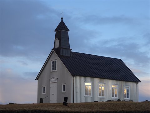 White wooden church under dusk sky, lit windows, grass in front