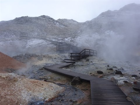 Wooden walkway between fumaroles and mineral mountains, geothermal steam in diffuse light