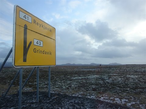 Yellow road sign to Reykjavik and Grindavik under a cloudy sky