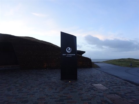 Dark sign on stone plaza in front of rocky structure, cloudy sky