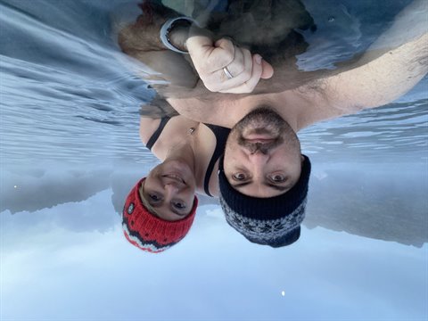 Couple in wool hats reflected in cold water, upside-down selfie, soft light