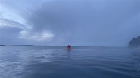 Swimmer in blue geothermal waters under cloudy sky, soft twilight light