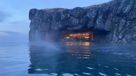 Bar inside a rocky sea cave, warm lights glowing over steaming blue water