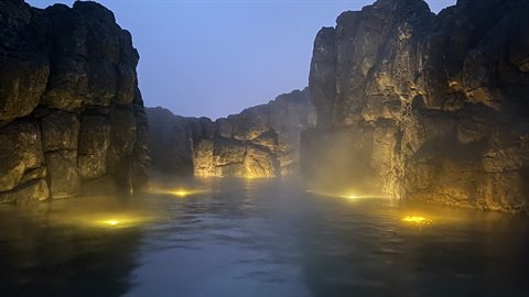 Steamy thermal water between illuminated rock walls, underwater lights at dusk