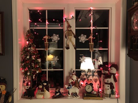 Indoor window decorated for Christmas with snowmen dolls, red lights and small tree
