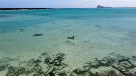 Fisher on small boat in turquoise lagoon, volcanic islet on horizon