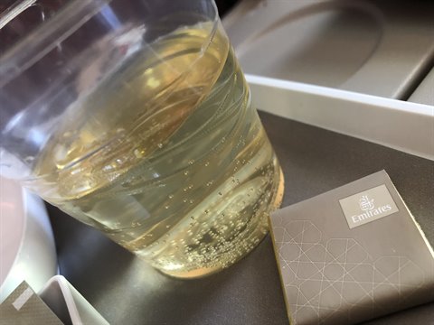 Plastic cup with sparkling drink and chocolate on tray table aboard a plane