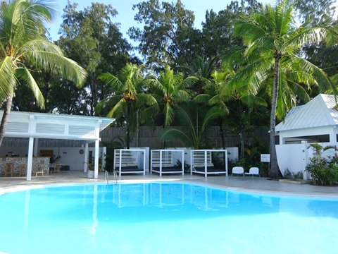 Turquoise pool with white cabanas among palm trees, bright sunlight, tropical resort