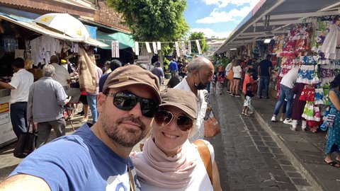 Couple takes selfie at an open-air market with clothing stalls