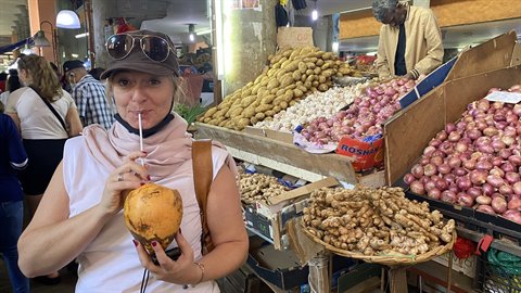 Traveler in cap sips from a coconut among onion stalls at covered market