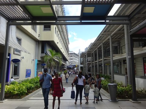 Pedestrians walking under a colorful metal canopy between commercial buildings, daylight