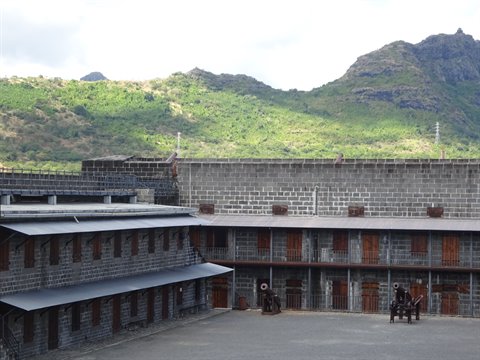 Stone fortress courtyard with historic cannons, green hills under cloudy sky