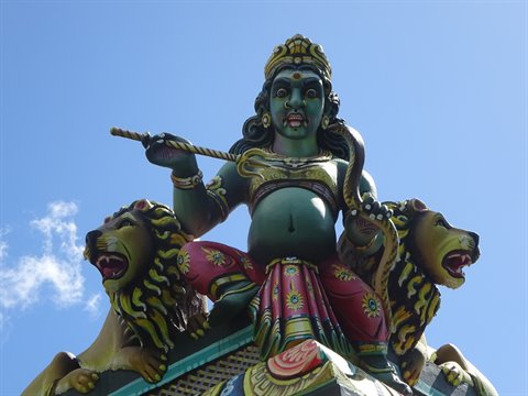 Colorful statue of deity with lions on a Hindu temple, blue sky, daylight