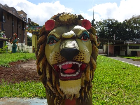 Painted lion statue on grass in front of a temple, daylight