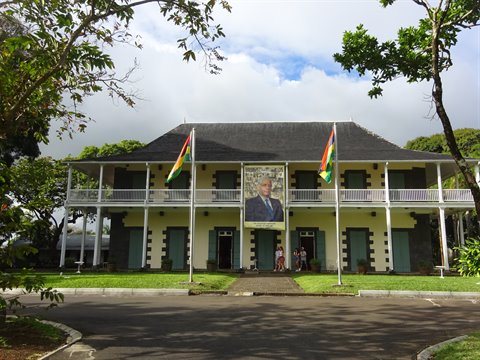 Tourists before a white colonial building with flags and portrait, daylight