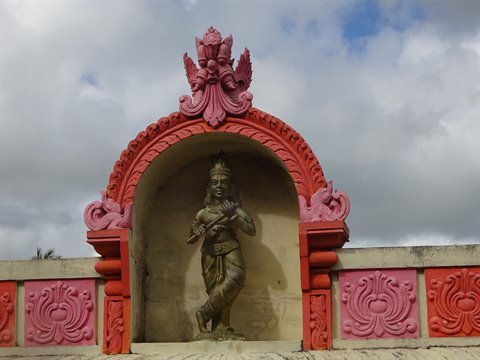 Deity statue in ornate red and pink niche, cloudy daylight