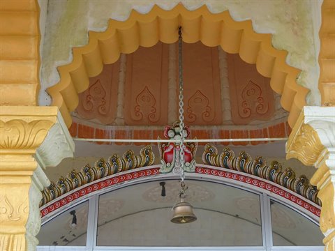 Bell hanging on a chain beneath a decorated yellow arch, natural light