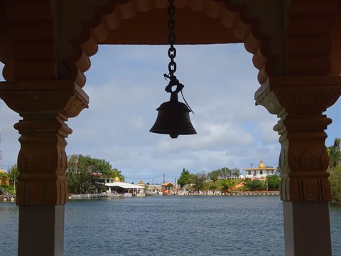 Bell hanging on a chain under a temple arch overlooking the lake