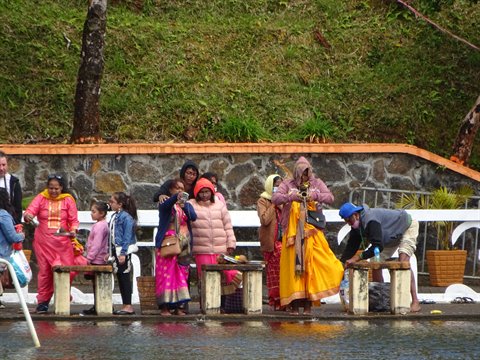 Women in colorful saris and tourists on a stone waterfront ledge, soft light