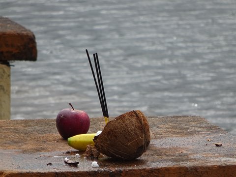 Apple, banana and coconut with incense sticks on a stone altar by the water