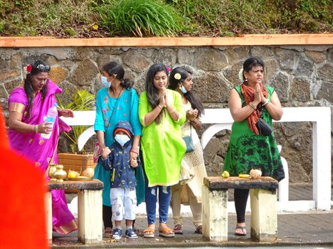 Women in saris pray with joined hands before offerings on stone altars