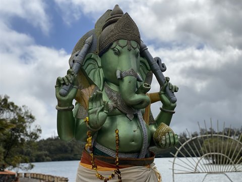 Green Ganesha statue by a lake, daylight cloudy, tourist site