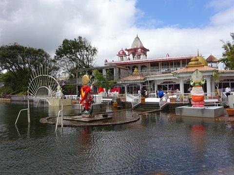 Colorful religious statues in the lake before a white temple, cloudy light