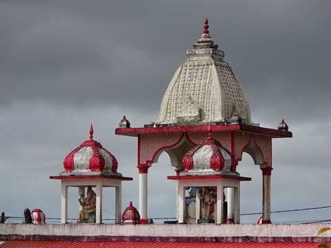 Hindu temple with white and red domes, dark cloudy sky, statues in shrines