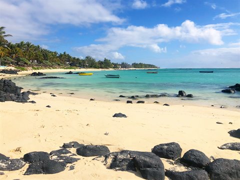Boat on pale sandy beach, volcanic rocks, palm trees, sunlight