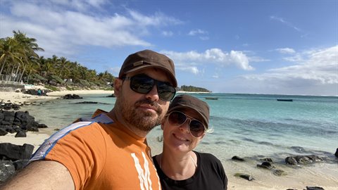 Couple takes a selfie on tropical beach, black rocks, turquoise sea, sunny light
