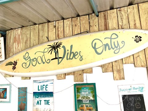 Yellow surfboard reading Good Vibes Only mounted on a wooden plank wall