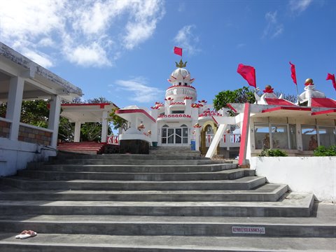 Concrete staircase leading to a white temple with red flags, blue sky with clouds