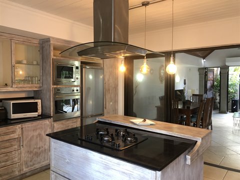 Whitewashed wooden kitchen with black island, steel hood and lit pendant lamps