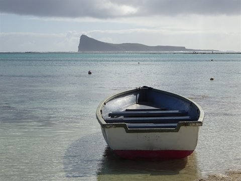 White wooden boat anchored in clear turquoise water, rocky headland under cloudy sky