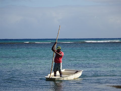 Man in hat pushing a white boat with a pole in turquoise water