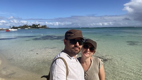 Couple in hats posing on the beach, turquoise sea, boat and clouds