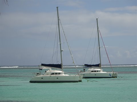 Two white catamarans anchored in turquoise water under a cloudy sky