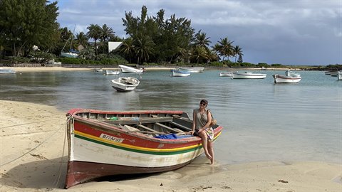 Woman sitting on a colorful wooden boat stranded on the beach, natural light