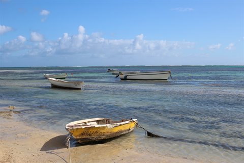 Fishing boats anchored in shallow sandy water under a partly cloudy sky