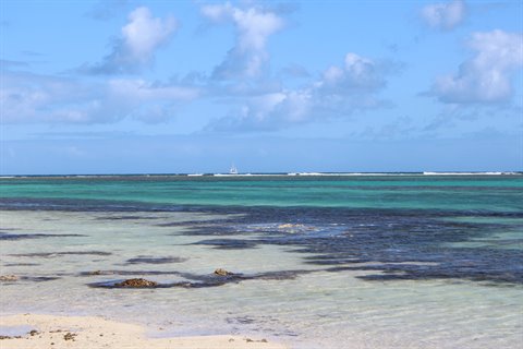 Turquoise lagoon with reef and white boat on horizon, sunlight