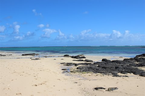 Pale sandy beach with black rocks, turquoise sea and blue cloudy sky