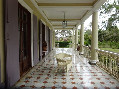 Colonial veranda with white columns, checkered marble floor and rattan armchair, natural light